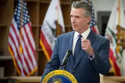 California governor speaking at podium with state seal and American flag in background