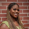 Woman with braided hair smiling against a red brick wall background