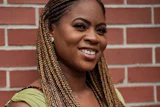 Woman with braided hair smiling against a red brick wall background