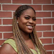 Woman with braided hair smiling against a red brick wall background