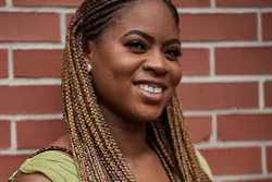 Woman with braided hair smiling against a red brick wall background