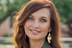 Professional portrait of a woman with reddish-brown wavy hair, pearl earrings, and pinstriped blazer smiling outdoors