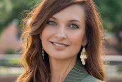 Professional portrait of a woman with reddish-brown wavy hair, pearl earrings, and pinstriped blazer smiling outdoors