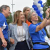 Group of people smiling while taking a selfie at an outdoor event decorated with blue and white balloons