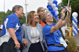 Group of people smiling while taking a selfie at an outdoor event decorated with blue and white balloons