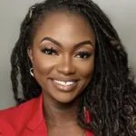 Professional headshot of a woman with long braided hair wearing a red blazer and smiling