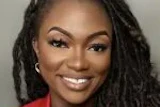 Professional headshot of a woman with long braided hair wearing a red blazer and smiling