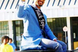 Man in blue blazer and sash waving from vehicle at outdoor event