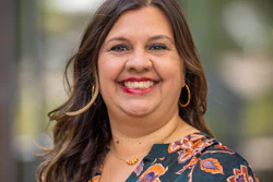 Professional headshot of a smiling woman wearing a floral patterned blouse with gold hoop earrings