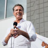 Man in white shirt speaking at microphone with California flag in background