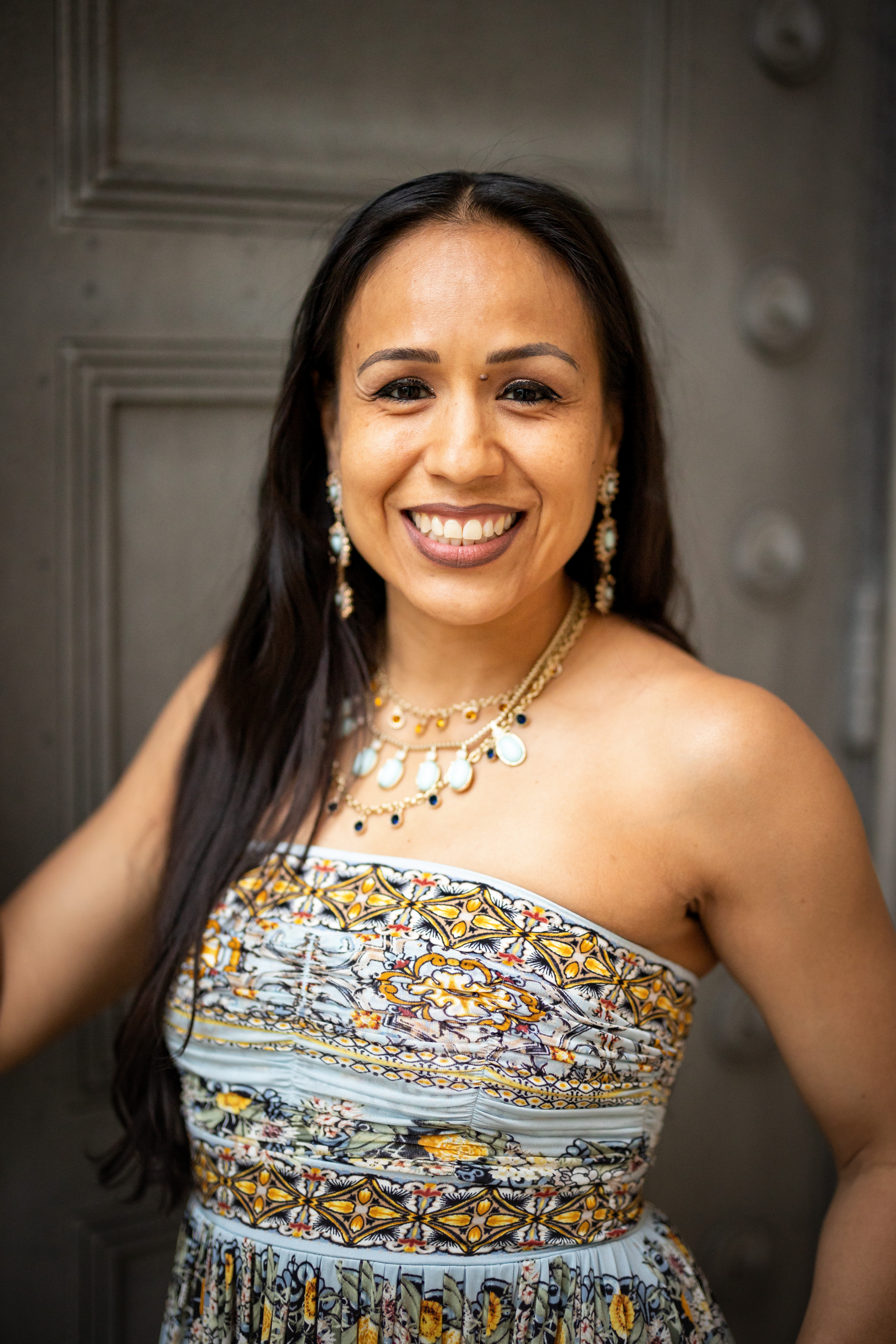 Professional portrait of a smiling woman wearing a patterned strapless dress and beaded necklace with pearl earrings