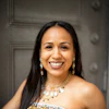 Professional portrait of a smiling woman wearing a patterned strapless dress and beaded necklace with pearl earrings