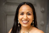 Professional portrait of a smiling woman wearing a patterned strapless dress and beaded necklace with pearl earrings