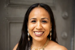 Professional portrait of a smiling woman wearing a patterned strapless dress and beaded necklace with pearl earrings