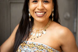 Professional portrait of a smiling woman wearing a patterned strapless dress and beaded necklace with pearl earrings