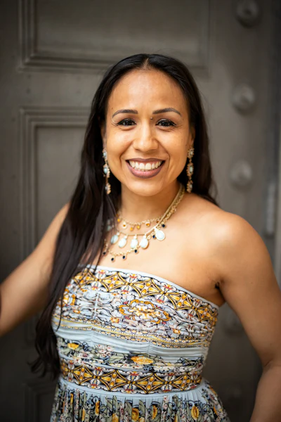 Professional portrait of a smiling woman wearing a patterned strapless dress and beaded necklace with pearl earrings