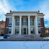 Classical brick building with white columns and blue windows on snowy campus grounds
