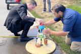 Two men assembling a wooden circular platform with colored mechanical components during an outdoor demonstration or workshop event.