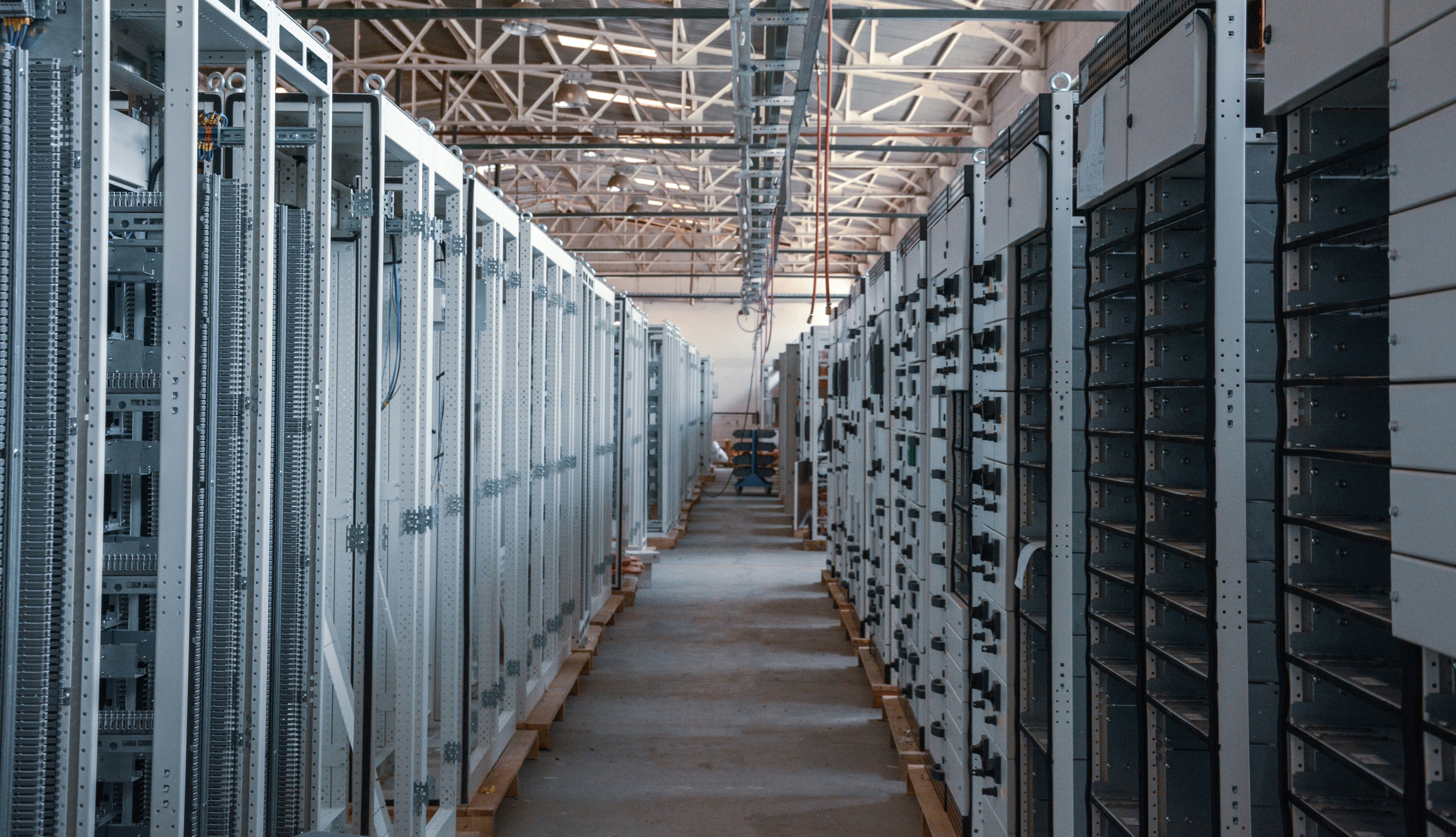 Industrial electrical substation with rows of white and black control cabinets and distribution panels in a warehouse facility