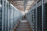 Industrial electrical substation with rows of white and black control cabinets and distribution panels in a warehouse facility