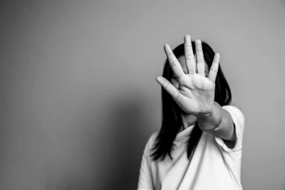 Person with hand raised in stop gesture, face obscured, black and white portrait
