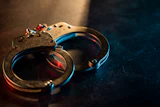 Metal handcuffs with blue and red lighting on dark textured surface