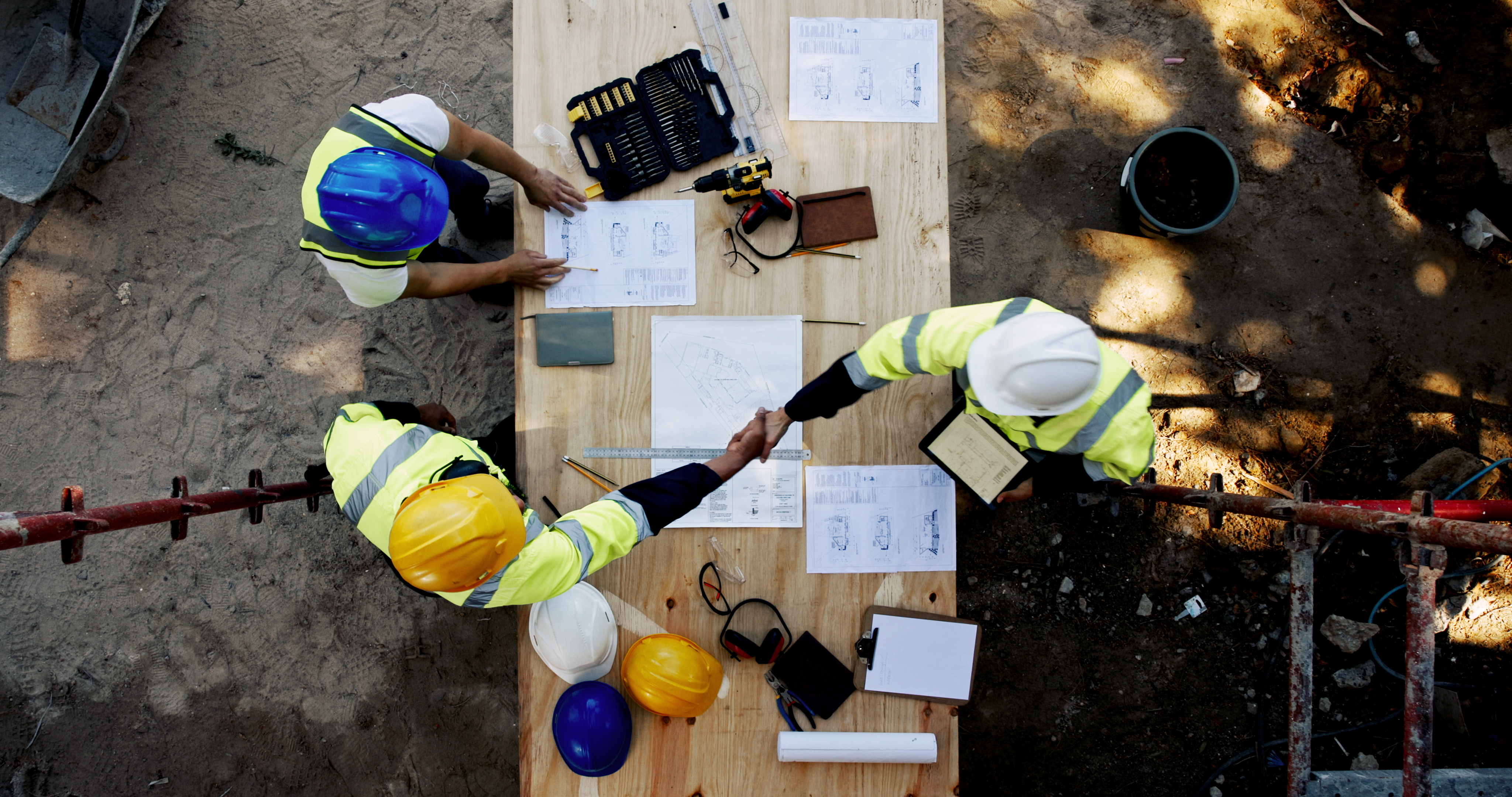 Overhead view of construction workers reviewing blueprints on wooden platform with safety equipment