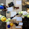 Overhead view of construction workers reviewing blueprints on wooden platform with safety equipment