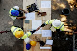 Overhead view of construction workers reviewing blueprints on wooden platform with safety equipment
