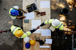 Overhead view of construction workers reviewing blueprints on wooden platform with safety equipment