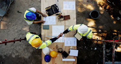 Overhead view of construction workers reviewing blueprints on wooden platform with safety equipment