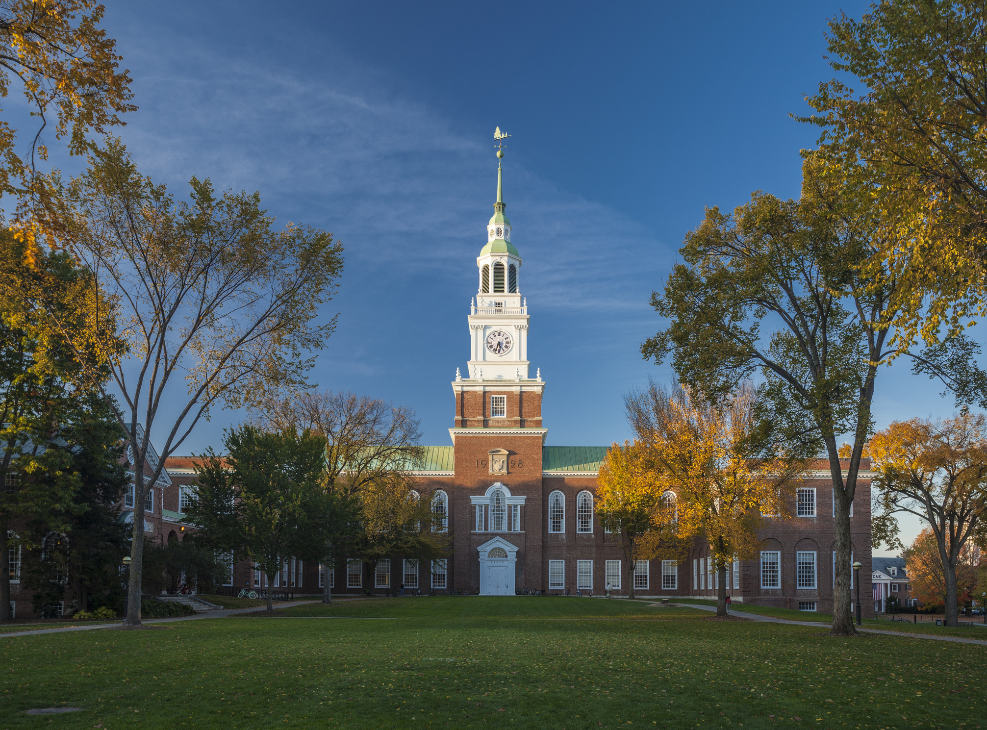 Historic red brick building with white steeple and clock tower surrounded by autumn trees on manicured green lawn