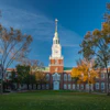Historic red brick building with white steeple and clock tower surrounded by autumn trees on manicured green lawn
