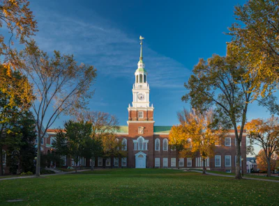 Historic red brick building with white steeple and clock tower surrounded by autumn trees on manicured green lawn