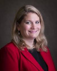 Professional headshot of a woman with shoulder-length blonde hair wearing a red blazer and dark top