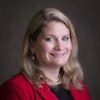 Professional headshot of a woman with shoulder-length blonde hair wearing a red blazer and dark top