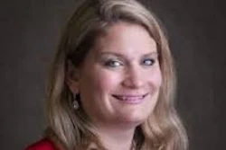 Professional headshot of a woman with shoulder-length blonde hair wearing a red blazer and dark top