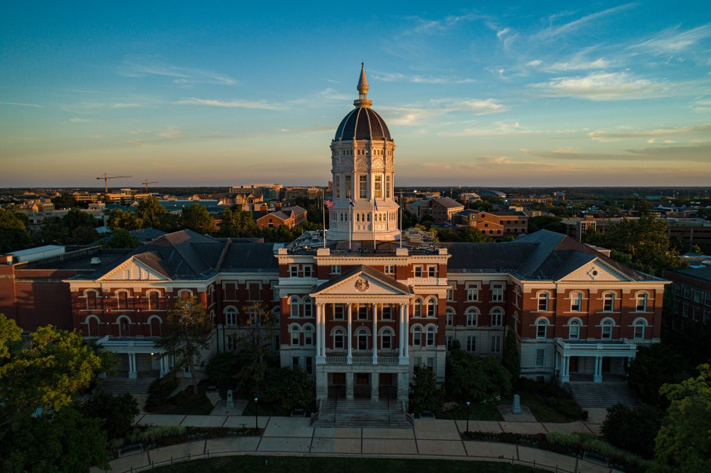 Golden dome university building with red brick architecture and symmetrical wings photographed at sunset