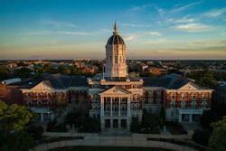 Golden dome university building with red brick architecture and symmetrical wings photographed at sunset