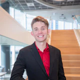 Young professional man in black blazer and red shirt smiling in modern office stairwell