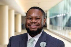 Professional man in dark blazer and gray shirt smiling in modern office corridor