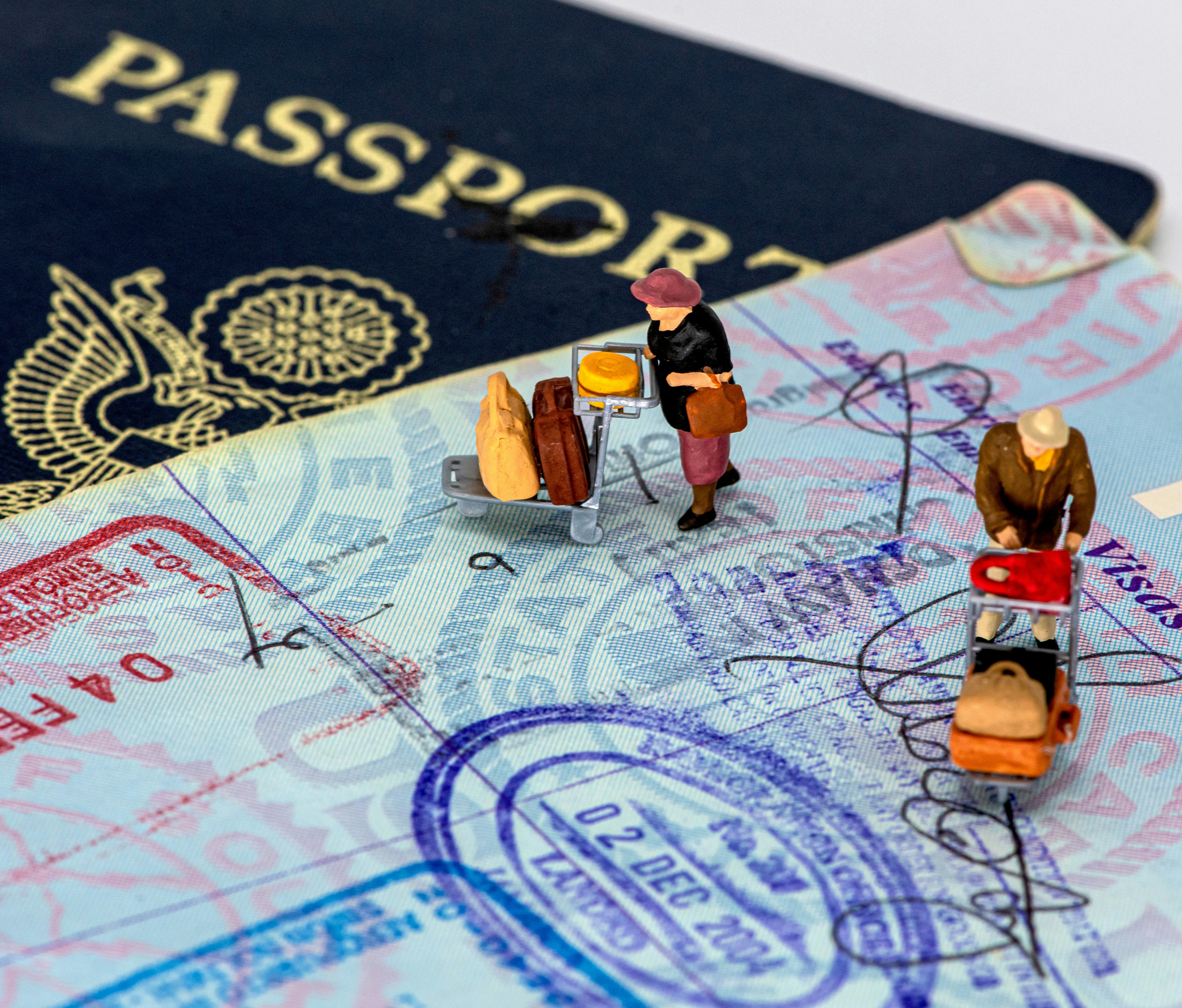 Miniature travelers with luggage positioned on passport pages and currency, illustrating international travel and immigration concepts