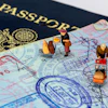 Miniature travelers with luggage positioned on passport pages and currency, illustrating international travel and immigration concepts