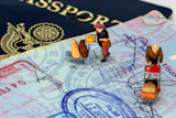 Miniature travelers with luggage positioned on passport pages and currency, illustrating international travel and immigration concepts