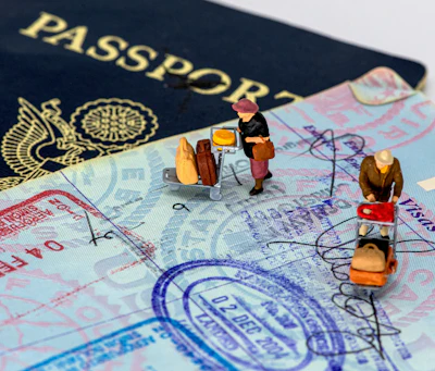 Miniature travelers with luggage positioned on passport pages and currency, illustrating international travel and immigration concepts