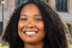 Professional headshot of smiling woman with curly dark hair wearing black blazer and silver necklace