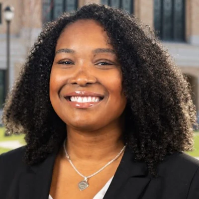 Professional headshot of smiling woman with curly dark hair wearing black blazer and silver necklace