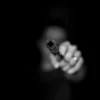 Person aiming handgun directly at camera in dramatic black and white photograph