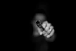 Person aiming handgun directly at camera in dramatic black and white photograph