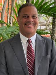 Professional headshot of man in gray suit and burgundy striped tie smiling at camera